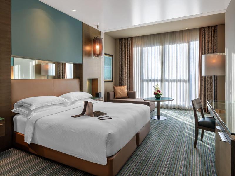 Modern hotel room with double bed, seating area, and large window with curtains.