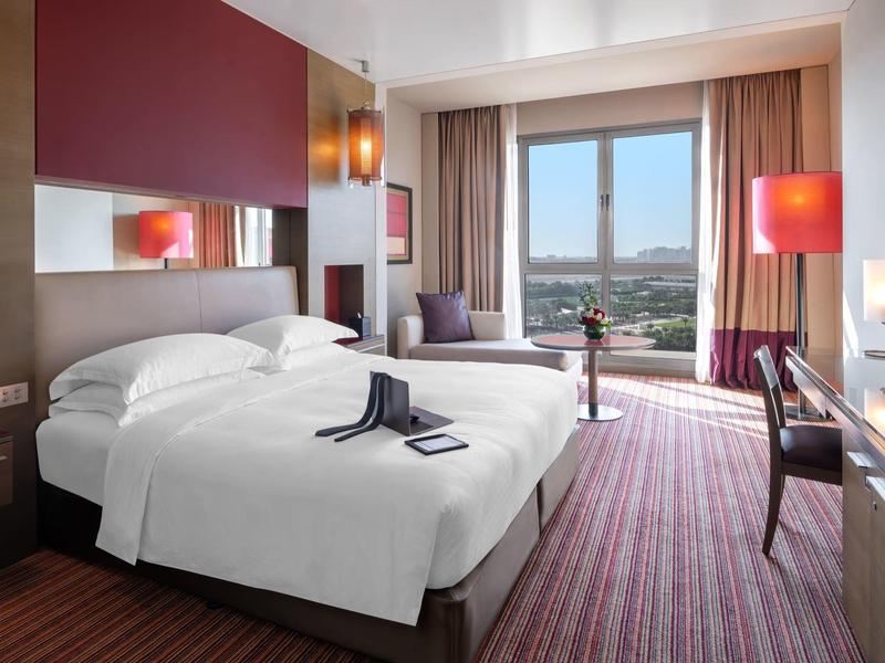 Modern hotel room with two single beds, city view, and warm lighting.