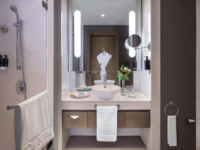 Modern bathroom with sink, mirrors, towels, and shower in a hotel room.