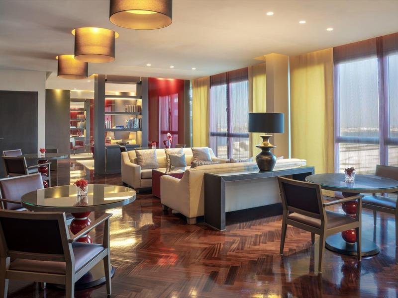 Bright hotel lounge with armchairs, sofas, and large windows overlooking the city.