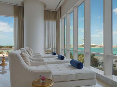 Helle Lounge mit weißen Sesseln, blauen Kissen und großen Fenstern mit Meerblick.
