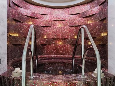 Rundes Mosaik-Becken mit Edelstahlgeländern, eingebettet in eine pink glänzende Wandgestaltung.