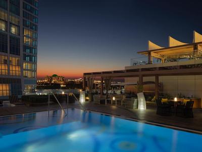 Beleuchteter Pool auf der Dachterrasse mit Stadtblick bei Sonnenuntergang und dämmerndem Himmel.