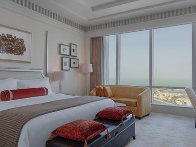 Helles Hotelzimmer mit großem Bett, roter Dekoration, Ledersofa und Panoramafenster mit Aussicht.