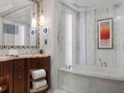 Helles Badezimmer mit Marmorwänden, großer Badewanne, Holzschrank und Spiegel mit Beleuchtung.