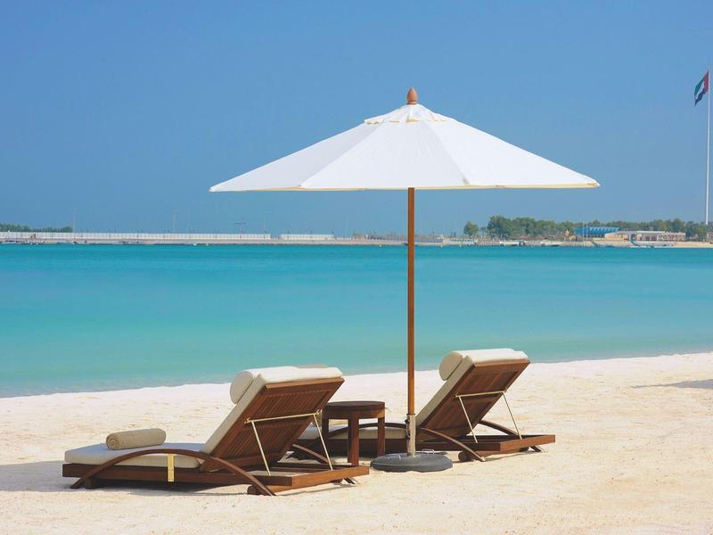 Dos tumbonas con sombrilla en la tranquila playa arenosa frente al mar azul.