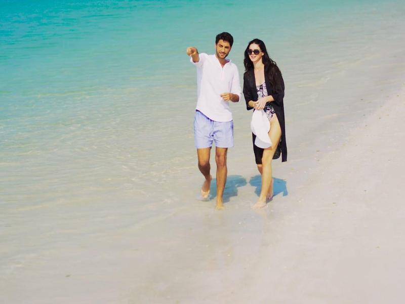 Pareja caminando por la playa de aguas turquesas, descalzos en agua poco profunda, ambiente relajado