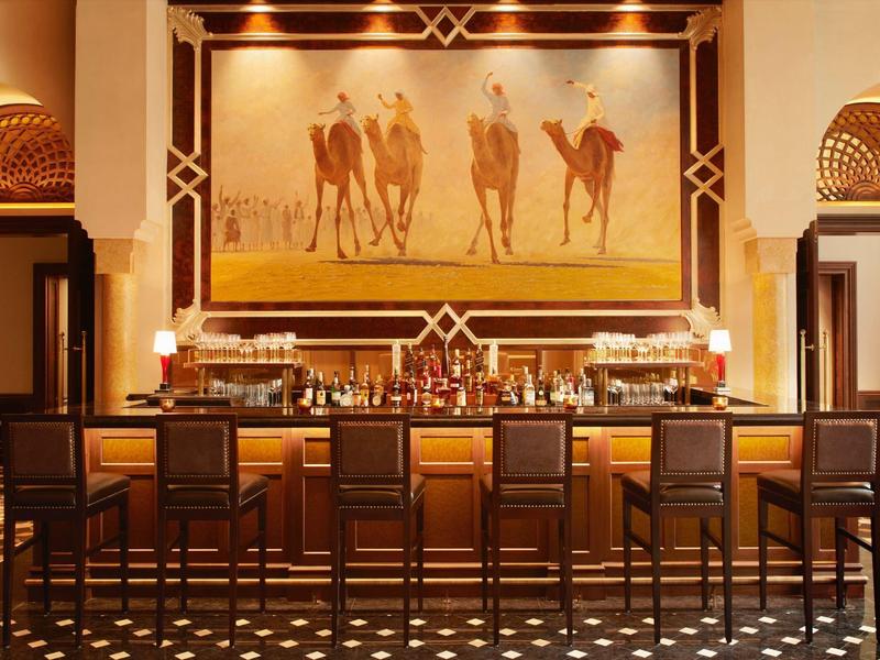 Bar elegante de hotel con sillas de madera y gran cuadro de jinetes de camellos en la pared.