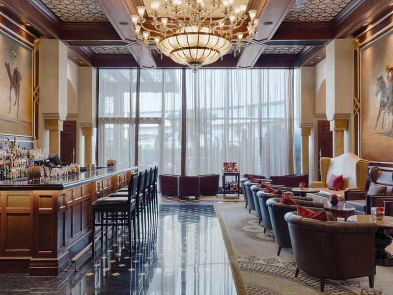 Elegante sala de hotel con bar, candelabro y grandes ventanas con vista al exterior.