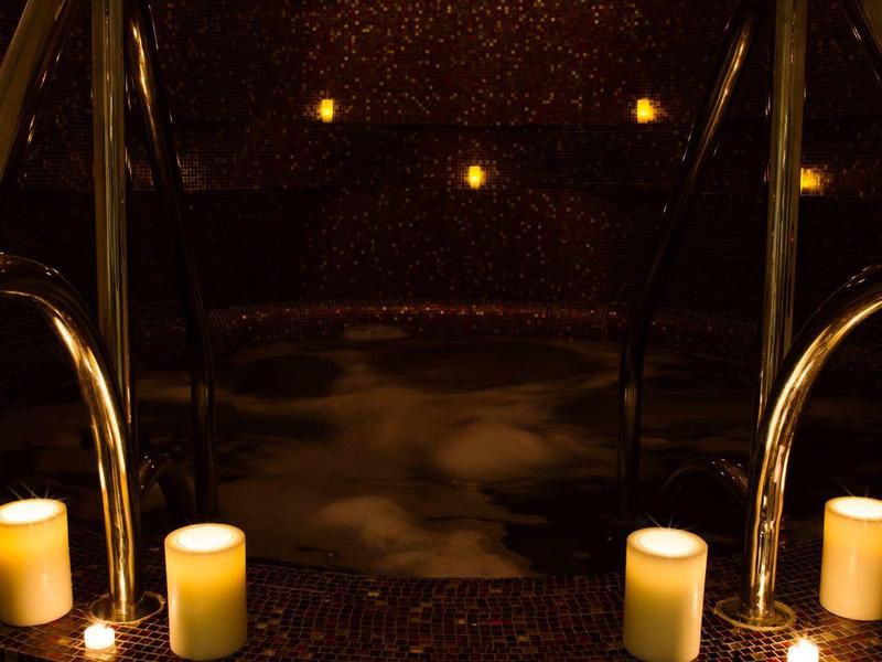 Piscina de bienestar semioscura con velas y barandales metálicos en ambiente tranquilo.