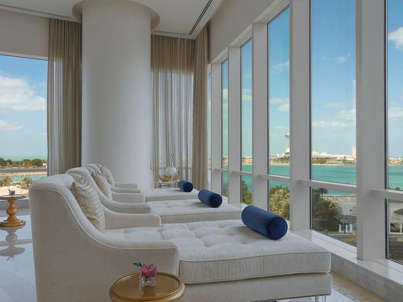 Salón luminoso con tumbonas blancas y vistas al mar a través de grandes ventanales.