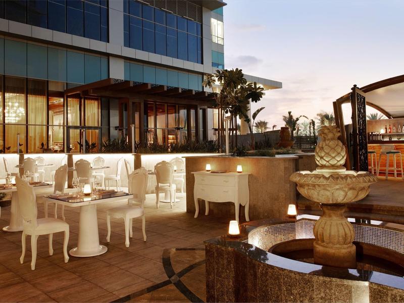 Terraza de un hotel con mesas, sillas y una fuente al atardecer.