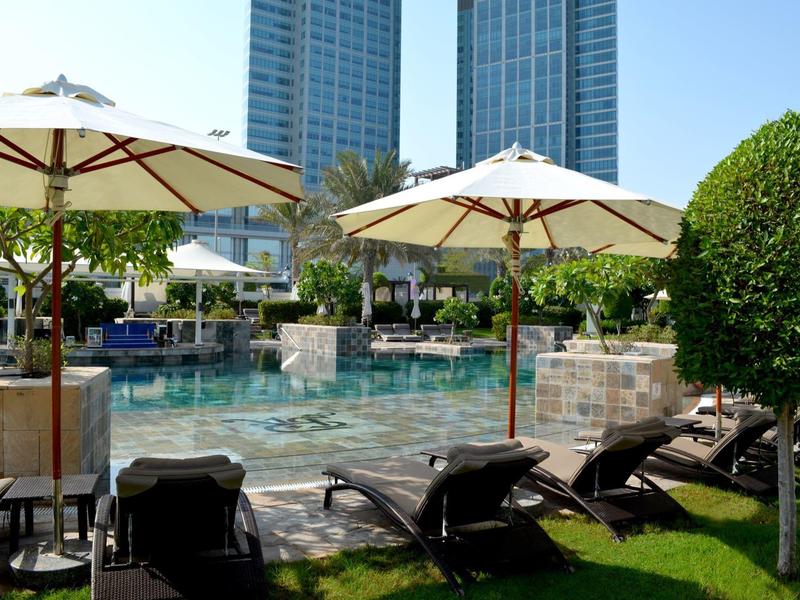 Área de piscina con tumbonas y sombrillas junto a altos edificios de hotel en un día soleado