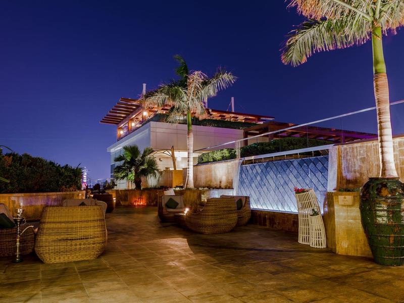 Área exterior de una terraza de hotel moderna por la noche con asientos y palmera.