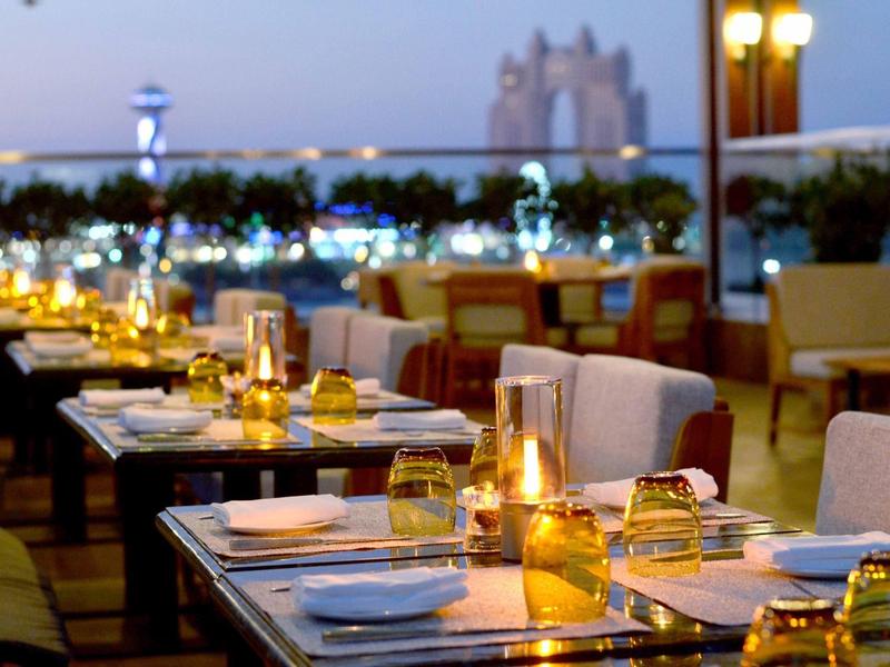 Terraza de restaurante al atardecer con mesas preparadas y luces cálidas para cenar al aire libre.