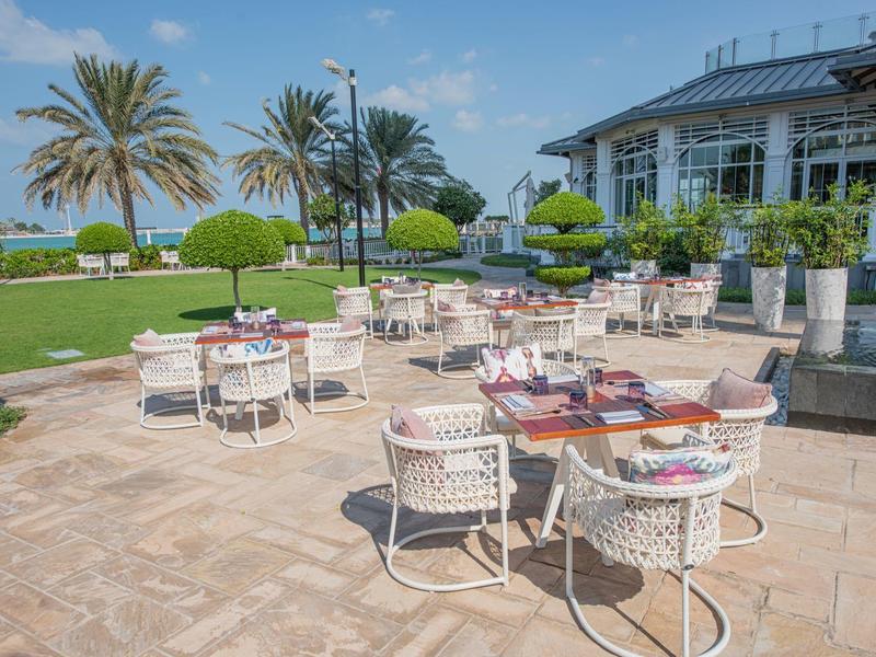 Terraza con mesas y sillas frente a un hotel con vista al jardín y al mar.