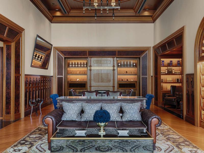 Sala elegante con sofá de cuero, estanterías de madera y acentos decorativos en tonos cálidos.