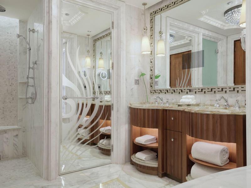 Baño elegante con mármol, lavabo doble, armarios de madera y ducha de vidrio en una habitación de hotel.