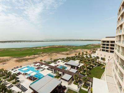 Hotel complex with pool and view over a large lake with natural landscape in the background.