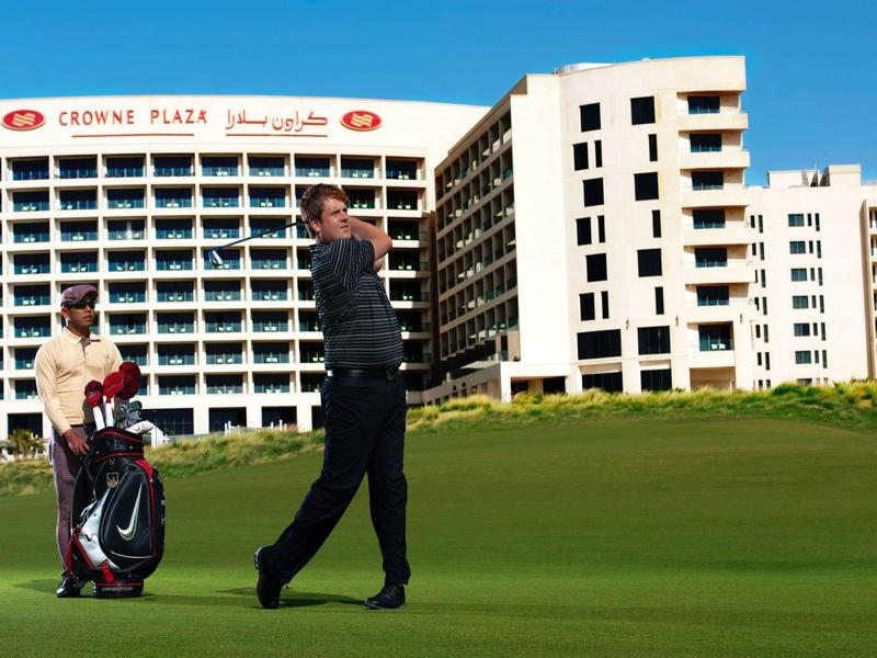 Zwei Männer auf gepflegtem Golfplatz vor mehrstöckigem Hotel mit klarem blauen Himmel.