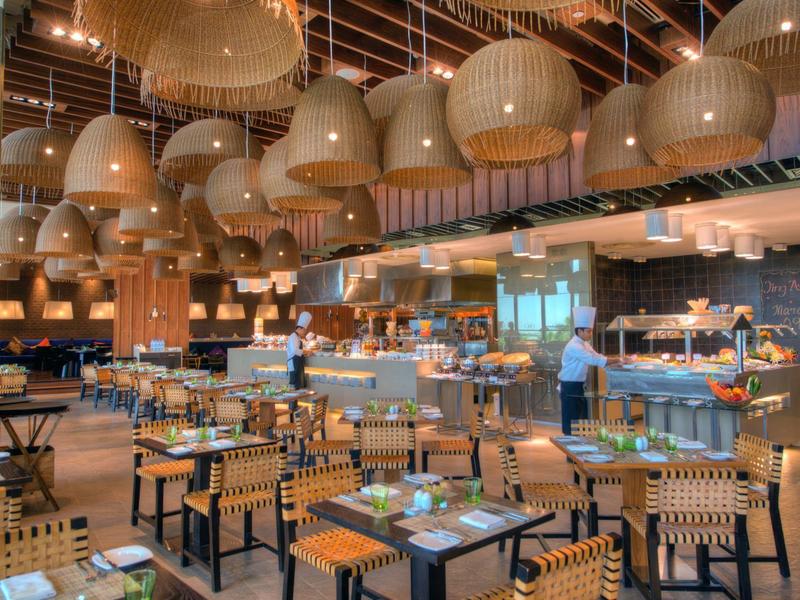 Moderner Restaurantinnenraum mit vielen Holztischen, Stühlen und großen, hängenden Lampen.