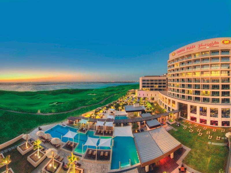 Luxushotel mit großen Pools, Liegen und grüner Landschaft bei Sonnenuntergang.