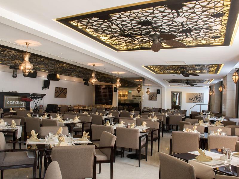 Großes, modernes Restaurant mit vielen gedeckten Tischen und dekorativer Deckenbeleuchtung.