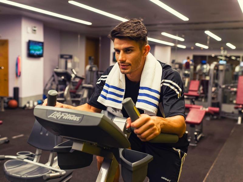 Ein Mann trainiert auf einem Crosstrainer in einem modernen Fitnessstudio mit Geräten im Hintergrund.