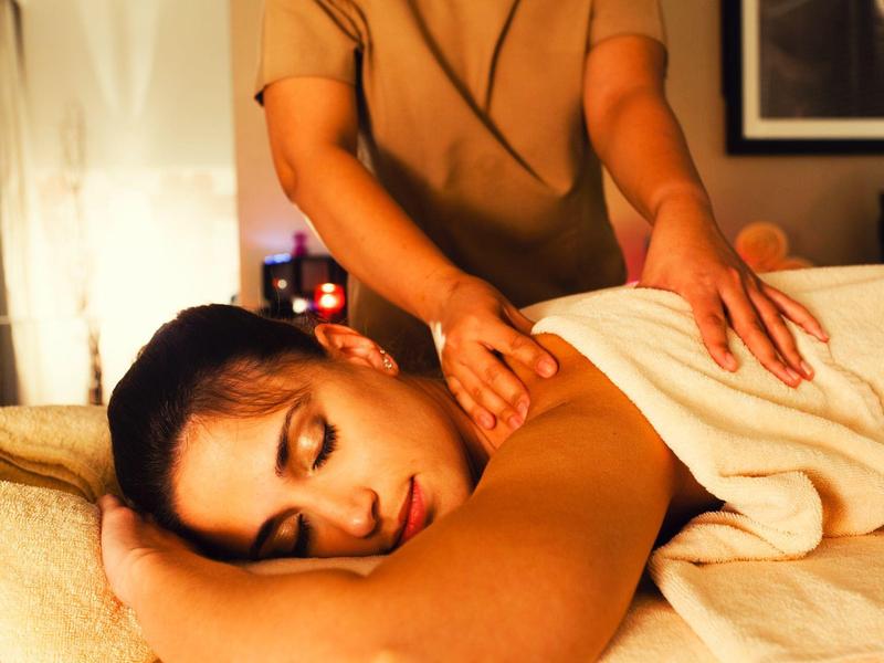 Frau entspannt auf Massagetisch mit braunem Tuch, Massage durch Hände, gedämpftes warmes Licht.