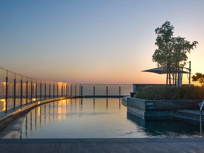 Piscina en la azotea con barandilla de vidrio y árbol al atardecer sobre una ciudad.