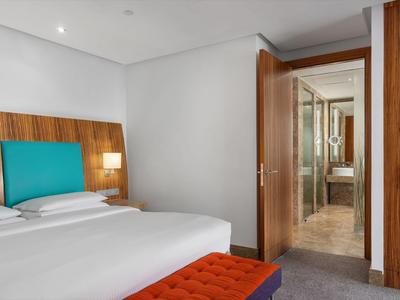 Habitación de hotel moderna con cama doble, cabecero turquesa y acceso al baño.