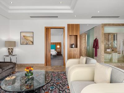 Sala de estar moderna con sofá beige, mesa de centro de vidrio y vista a habitaciones contiguas.