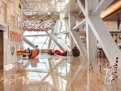 Área de salón de hotel moderna y luminosa con grandes ventanales e impactante instalación en el techo.