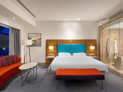 Habitación de hotel moderna con cama, sofá rojo y ducha de vidrio