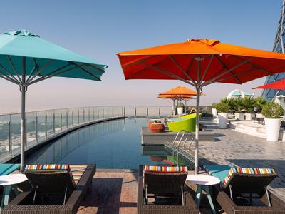 Piscina infinita en terraza en la azotea con sombrillas coloridas y tumbonas con vista a la ciudad