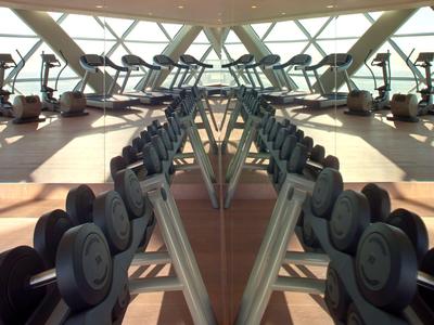 Fitnessraum mit Hanteln und Cardiogeräten in einem hellen, geräumigen Bereich mit großen Fenstern.