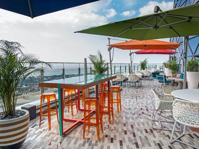 Terraza en la azotea con sombrillas coloridas, mesas, sillas y vista a la playa en un día soleado.