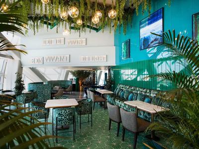 Café amueblado de forma moderna con paredes verdes, sillas acogedoras y plantas.