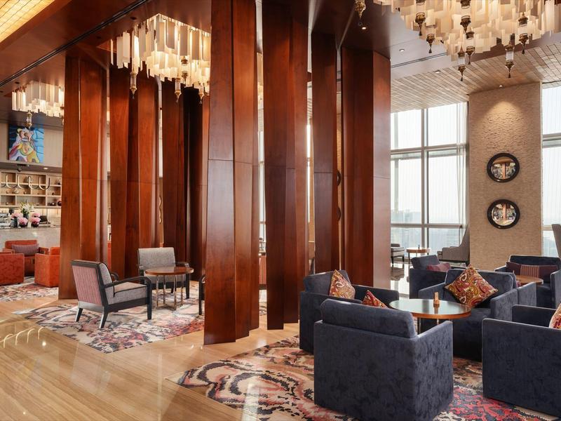 Área de salón elegante de hotel con pilares de madera, sillones, alfombras y candelabros.