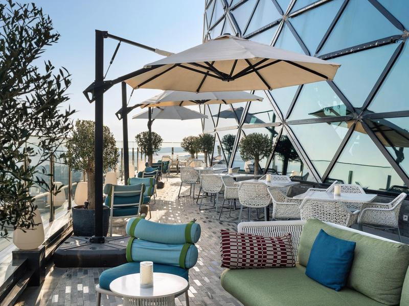 Terraza con muebles lounge modernos y sombrillas frente a una fachada de vidrio a plena luz del día.