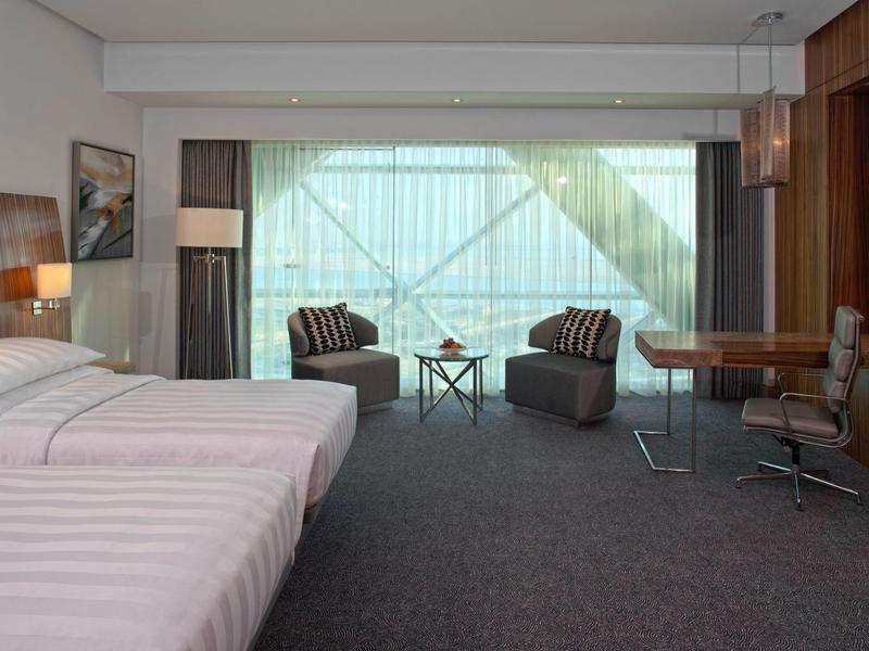 Habitación de hotel moderna con dos camas, sillones y ventana grande con cortinas