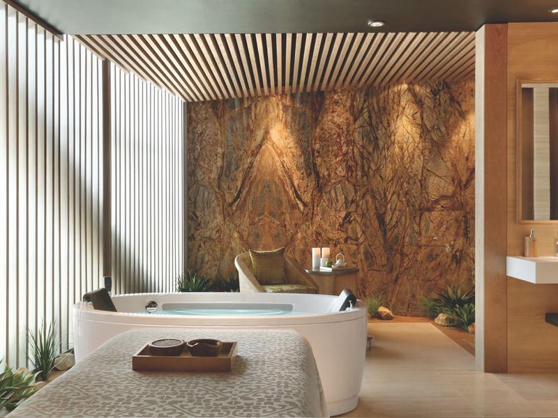 Baño moderno con bañera independiente, pared de piedra y camilla de masaje.