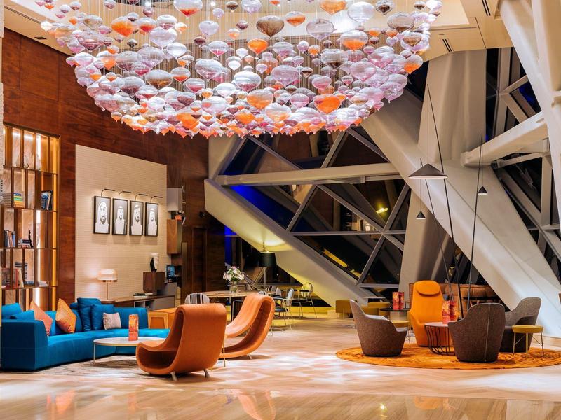 Un vestíbulo de hotel moderno con sillones coloridos y una iluminación decorativa en el techo con grandes pantallas.