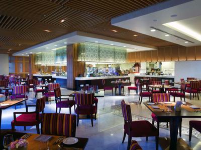 Modernes Hotelrestaurant mit vielen Tischen und gepolsterten Stühlen, warm beleuchtet.