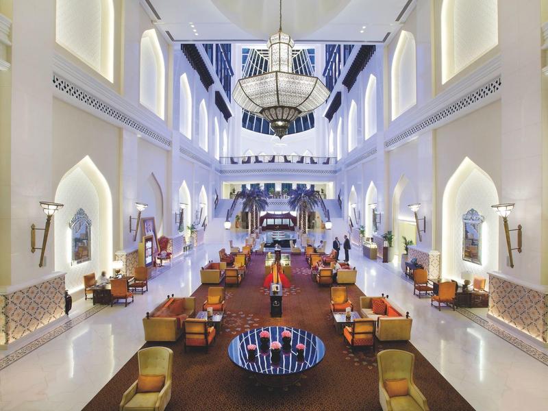 Großer heller Saal mit hohen Bögen, Kronleuchter und bequemen Sesseln in symmetrischer Anordnung.