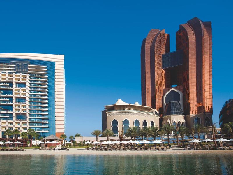 Moderne Stadtansicht mit hohem Glasgebäude, braunem Wolkenkratzer und Wasser im Vordergrund.