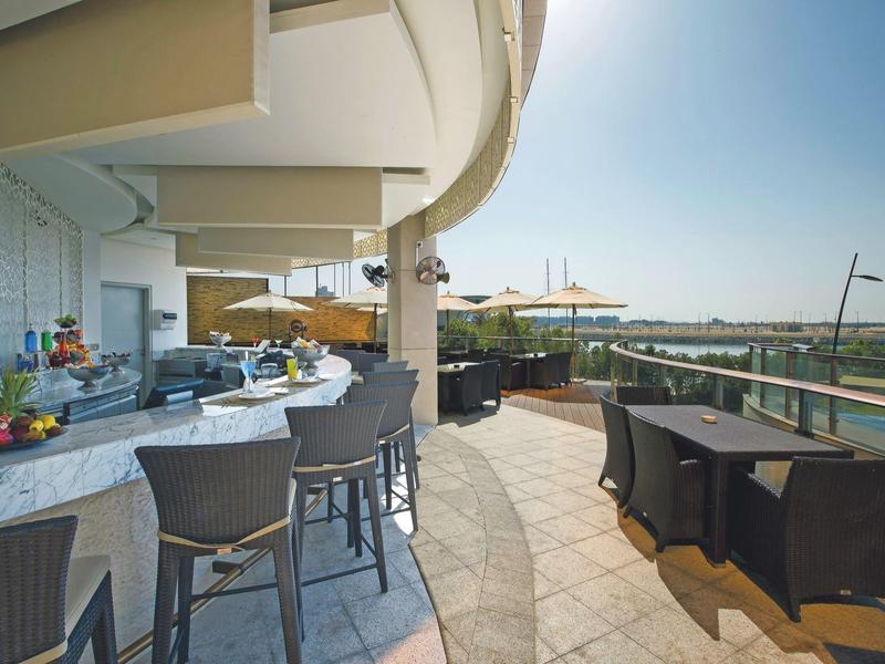 Große Terasse mit Bar, schwarzen Stühlen und Meerblick unter blauem Himmel.