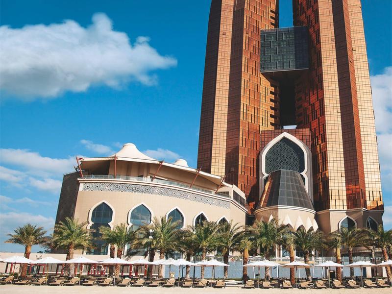 Hohe, orangefarbene moderne Architektur mit Palmen und blauem Himmel im Hintergrund.