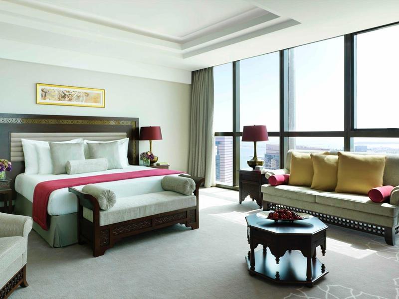 Modern eingerichtetes Wohnzimmer mit großen Fenstern, Sofa, Sesseln und dekorativem Hocker.