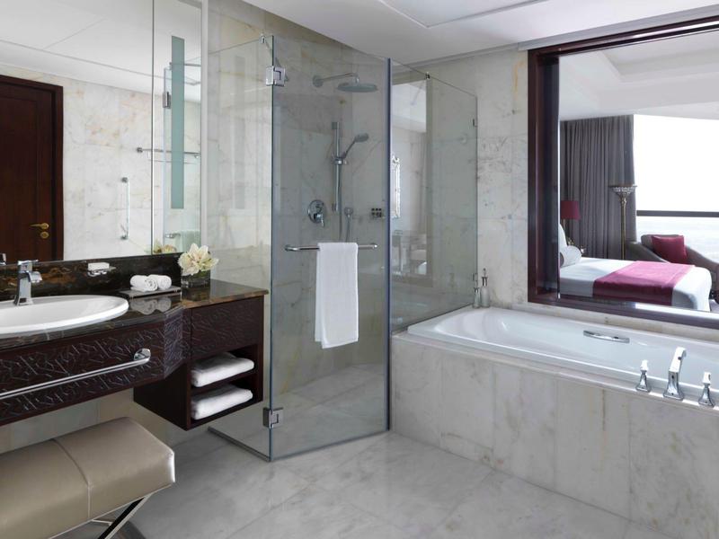 Modernes Badezimmer mit großer Badewanne, Glasdusche, dunklem Waschtisch und großem Spiegel.